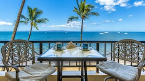 A table with two chairs, a view of the ocean, and palm trees.