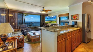 A modern kitchen with a large island, wooden cabinets, and a view of the ocean.