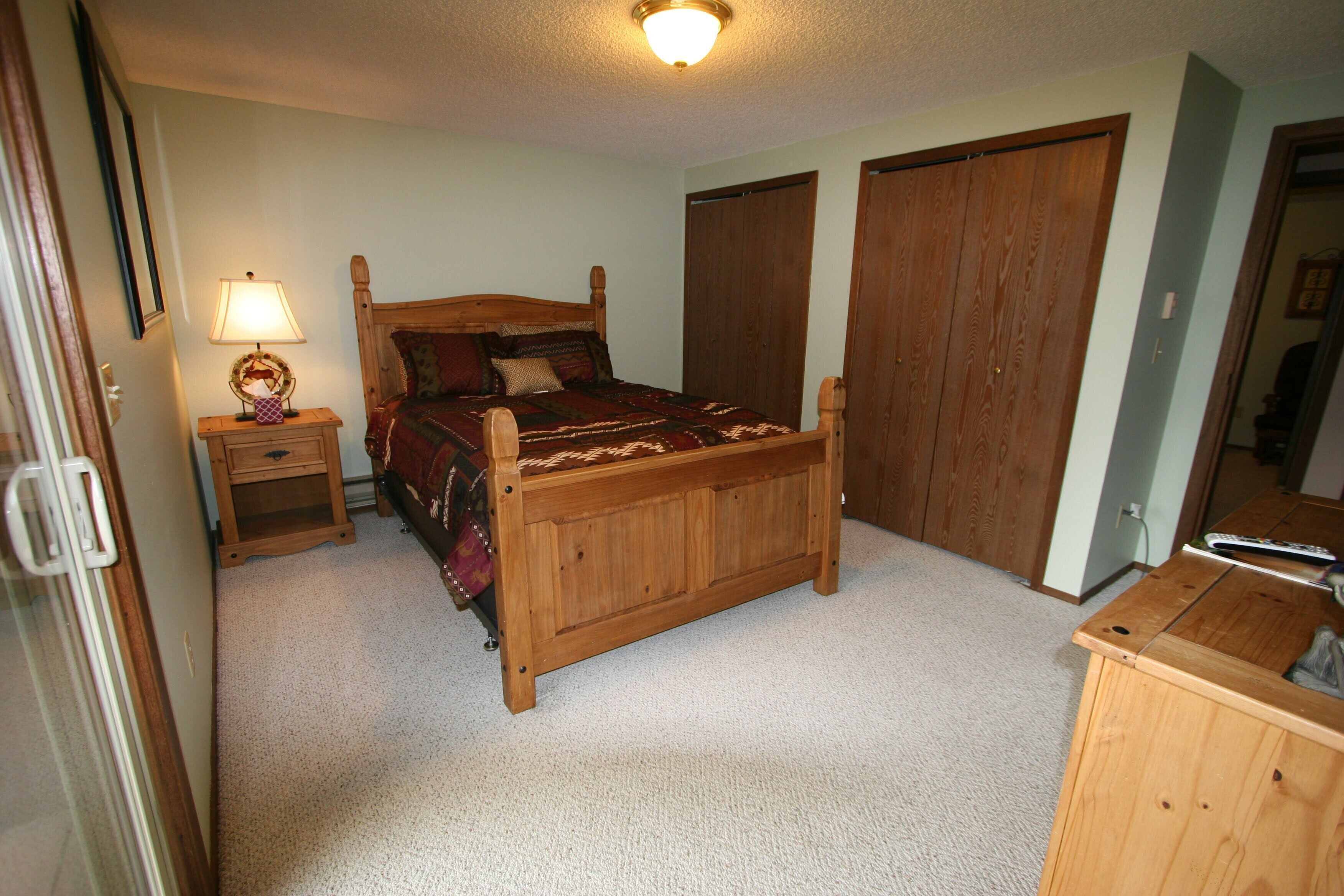Une chambre à coucher avec un lit en bois, une table de chevet avec une lampe et deux armoires en bois.