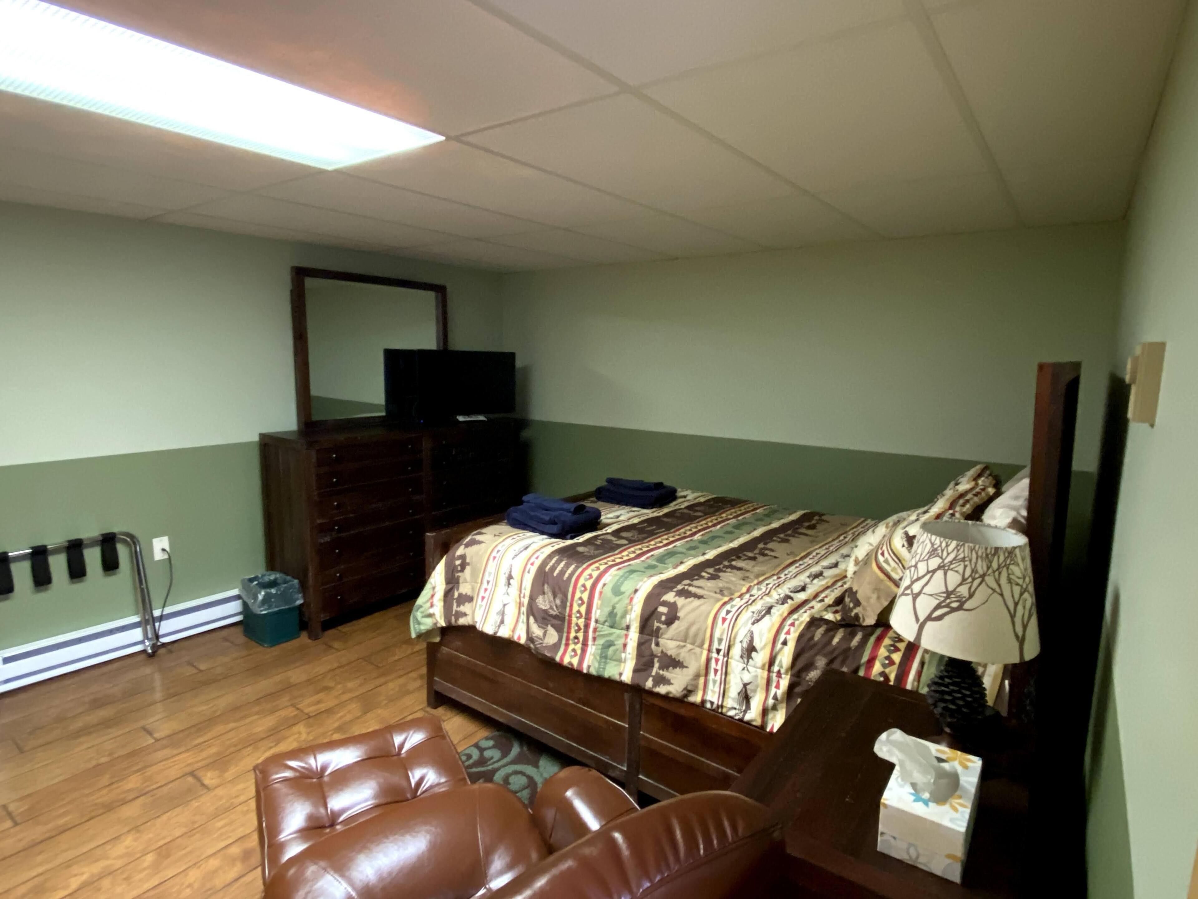 A bedroom with a bed, a dresser, a television, and a desk with a lamp and tissues.
