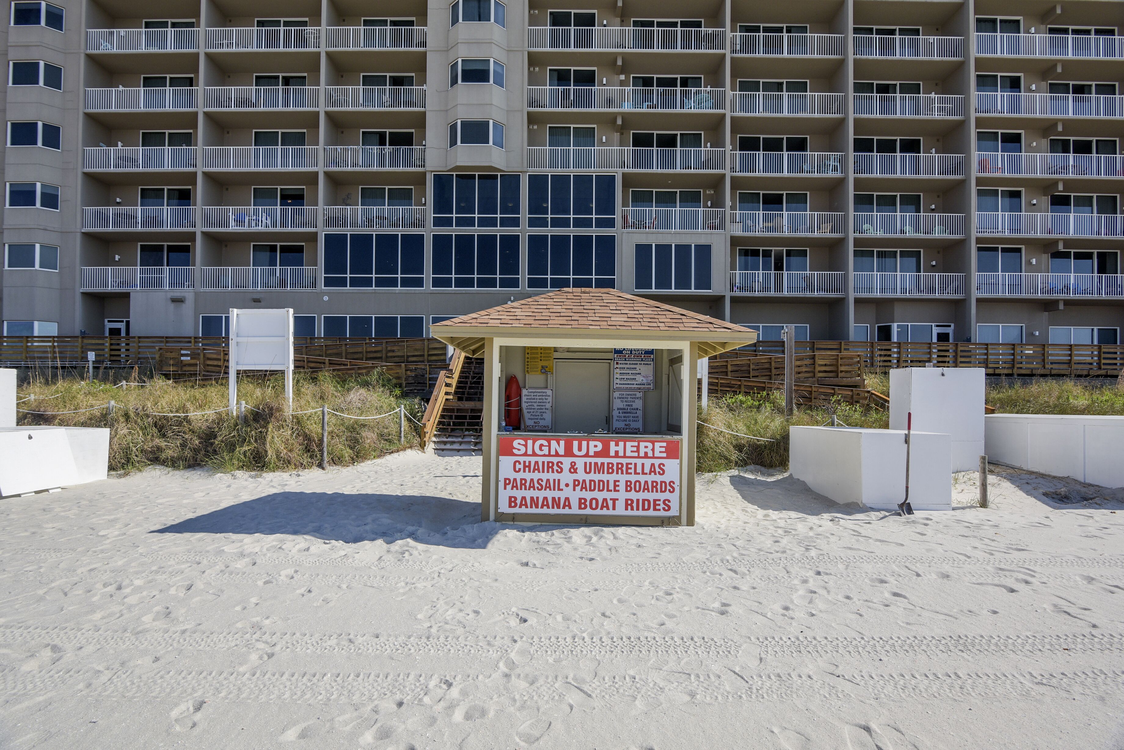 A beachside sign-up kiosk with a sign listing amenities like parasailing, paddle boards, and banana boat rides.