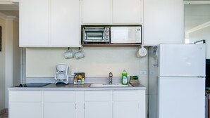 A kitchen with white cabinets, a built-in microwave, a coffee maker, and a refrigerator. - 〰Waikiki〰Studio w/Spectacular Views & Balcony-WAIKIKI GRAND HOTEL® 712 (Honolulu)