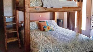 A rustic wooden bunk bed with a ladder, a ceiling fan, and patterned bedding.