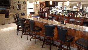 Een bar met een granieten aanrecht, barstoelen en diverse flessen drank.