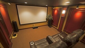 Een thuisbioscoopruimte met een groot scherm, leren loungestoelen en een vloerbedekking.
