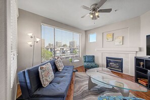 Una sala de estar moderna con un sofá, una mesa de centro de vidrio, una chimenea y vistas a la ciudad a través de amplios ventanales.