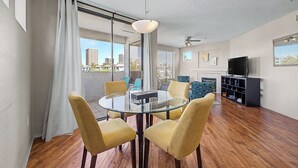 Un salon moderne avec une table à manger en verre, des chaises jaunes, un téléviseur et une vue sur la ville.
