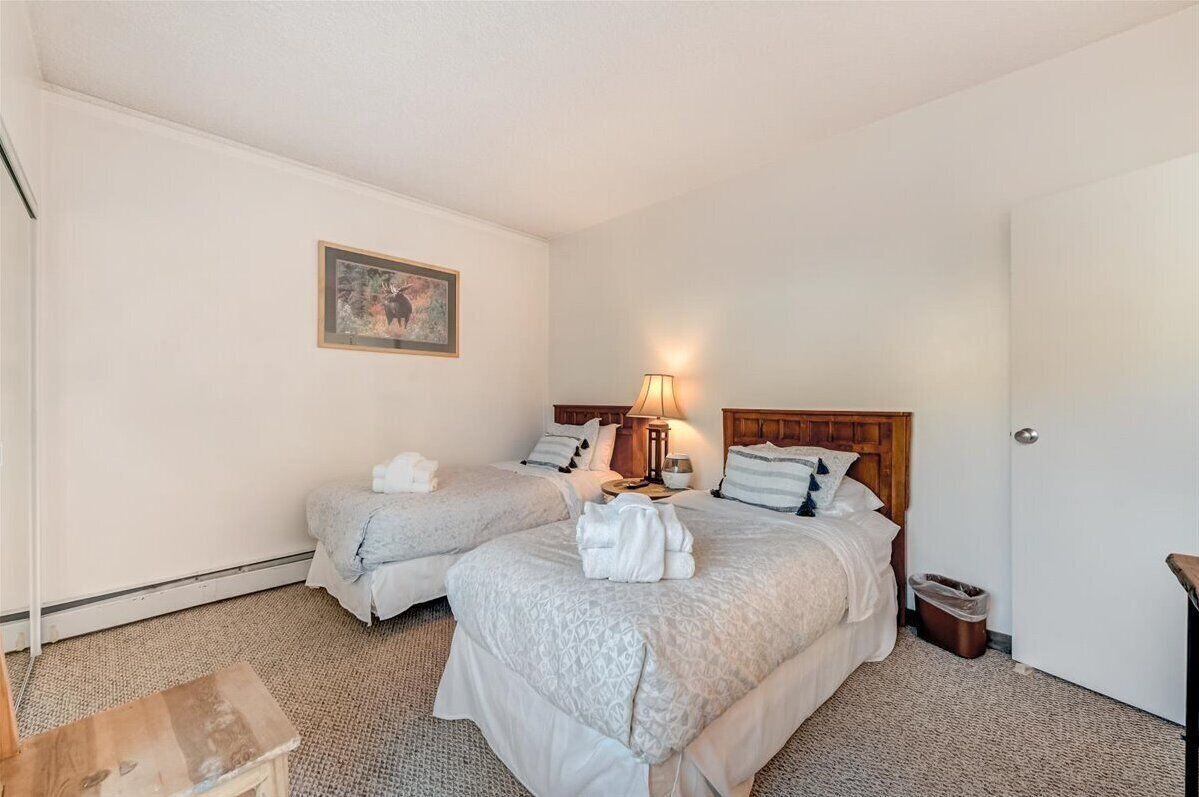 A hotel room with two beds, a nightstand, a lamp, a framed picture on the wall, and a door.