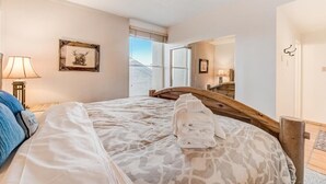 Een slaapkamer met een bed, een houten hoofdbord, een bedlampje, een lijst met een afbeelding en een raam met uitzicht.