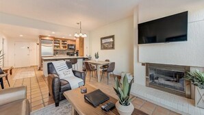 Een moderne woonkamer met een open haard, een flatscreentelevisie, een eethoek en een keuken op de achtergrond.