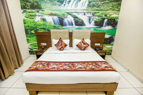 A neatly made bed with a floral bedspread, two pillows with a floral pattern, and a headboard with a waterfall mural. - Hotel Karan Residency (Amritsar)