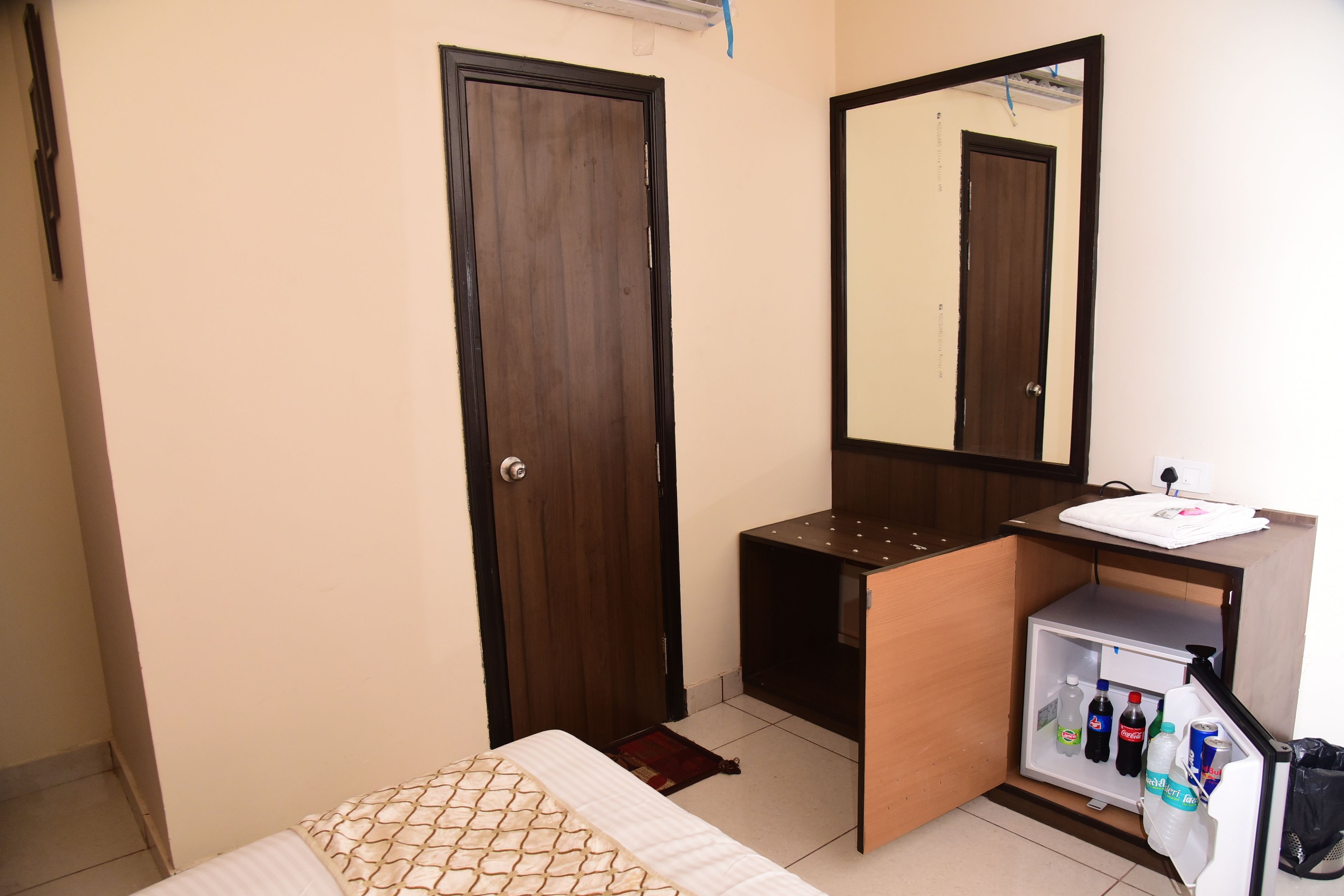 Une chambre comprenant un lit, une armoire, un miroir, un petit meuble avec un lavabo et un mini-réfrigérateur.