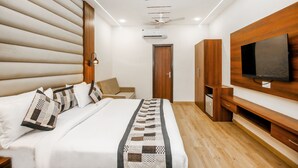 A modern hotel room with a large bed, wooden headboard, a flat-screen TV mounted on the wall, a ceiling fan, and an air conditioning unit.