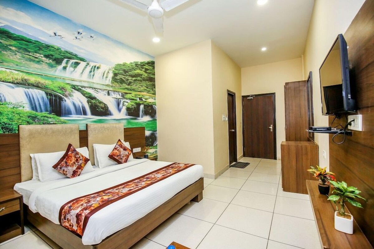 A hotel room with a large bed, a TV mounted on the wall, and a mural of a waterfall.