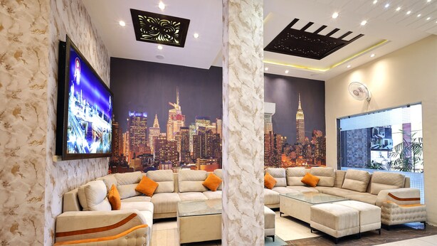 A modern living room with a cityscape mural, a flat-screen TV, and a sectional sofa with orange cushions.