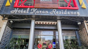 The exterior of Hotel Karar Residency with a modern facade, large windows, and a prominent entrance with steps leading up to it.
