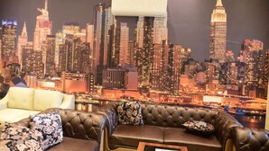 A room with a cityscape view, a brown leather sofa, and a white armchair.