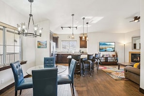 A spacious living area with a dining table, chairs, a sofa, a fireplace, and a kitchen in the background.