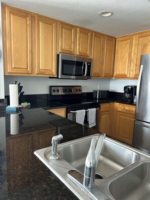 A kitchen with wooden cabinets, a stainless steel sink, a microwave, and a coffee maker.