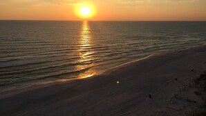A beach with a sunset over the ocean, sandy shore, and a few people in the distance. - Gulf Front Condo, Corner Unit, Stunning Views, Great Restaurants (Panama City Beach)