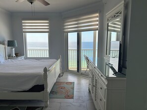 Un dormitorio con cama, cómoda, lámpara y vista al océano a través de amplias ventanas.