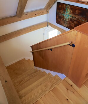 A wooden staircase with a handrail, wooden beams on the ceiling, and a painting on the wall.
