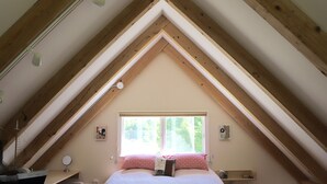 A bedroom with a sloped ceiling, a bed with pink bedding, a window, and wooden beams.