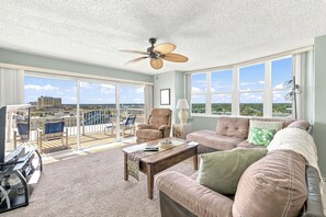A spacious living area with a balcony, a ceiling fan, and a view of the cityscape.