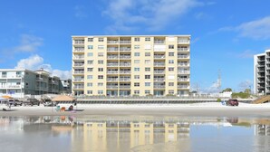 Un hôtel en bord de mer doté de nombreux balcons, une plage de sable en premier plan et un ciel dégagé.