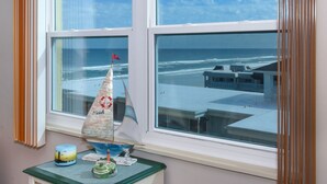 Une pièce dotée d’une grande fenêtre donnant sur l’océan, d’une petite table sur laquelle est posé un modèle de voilier, et d’un objet décoratif portant l’inscription « Plage ».
