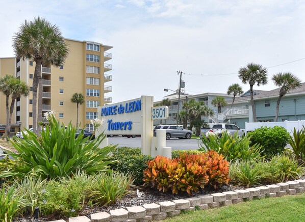 A sign for 'Ponce de Leon Towers' with a number '3501' and a view of a multi-story building with balconies and palm trees.