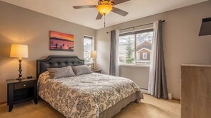 A bedroom with a large bed, two bedside tables with lamps, a ceiling fan, a window with curtains, and a painting on the wall. - Cozy 2BR/2BA Condo at Big Sky Resort (Big Sky)