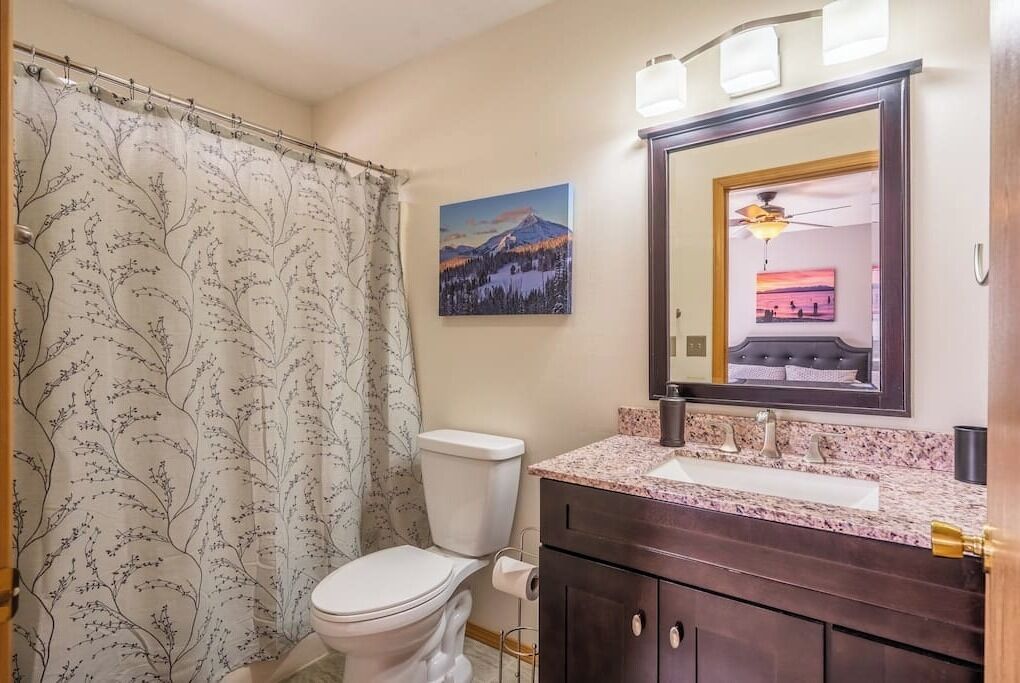 Un baño con inodoro, lavamanos y cortina de ducha con estampado de árboles.
