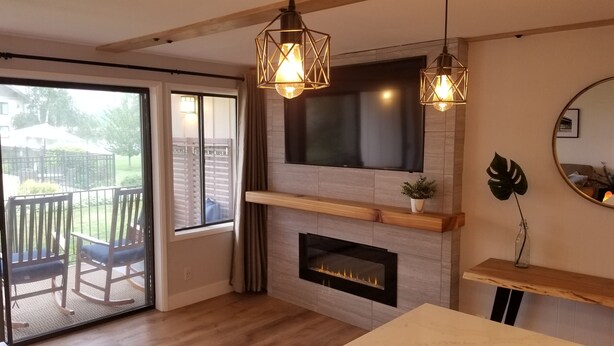 Ein modernes Wohnzimmer mit Kamin, einem an der Wand befestigten Fernseher und einem Balkon mit Gartenmöbeln.