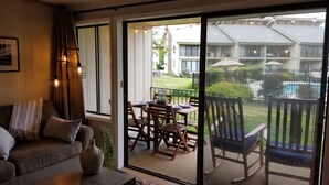 Ein gemütlicher Wohnbereich mit einer Couch, einem Esstisch für zwei Personen und einer Glasschiebetür, die auf einen Balkon mit Blick auf einen Pool führt.