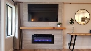 Ein modernes Wohnzimmer mit Kamin, einem Wand-Fernseher und einem runden Spiegel.