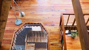 A wooden cabin with a wooden floor, a small desk with a chair, a birdcage, and a large window overlooking greenery.
