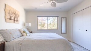 A bedroom with a large bed, a ceiling fan, a window with a view of trees, and a wardrobe.
