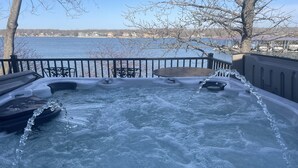 A hot tub with a control panel, surrounded by a metal railing, overlooking a body of water with buildings in the background. - Private Paradise spot !!  (Osage Beach)