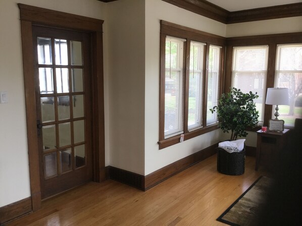 A hallway with wooden flooring, a door with glass panels, and windows with blinds.