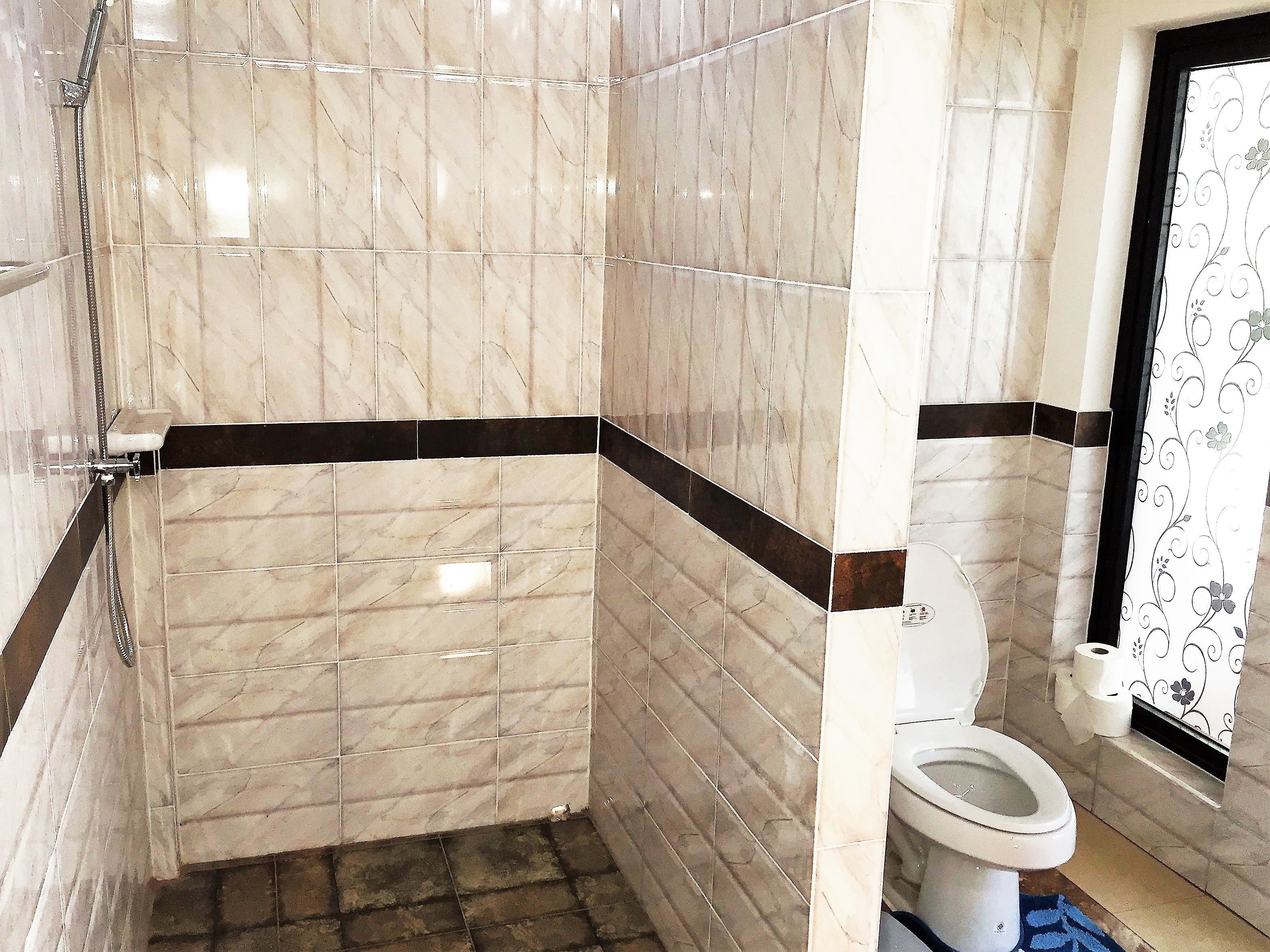 A bathroom with marble tiles, a shower, a toilet, and a patterned curtain.