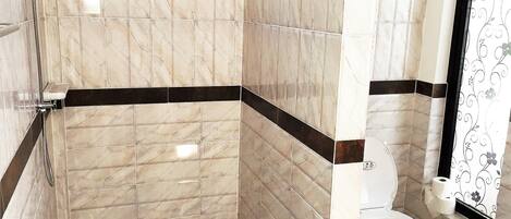 A bathroom with marble tiles, a shower, a toilet, and a patterned curtain.