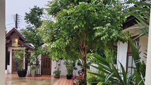 A courtyard with potted plants, a tiled floor, and a building with a traditional design. - Phu View Hideaway (Kantharalak)