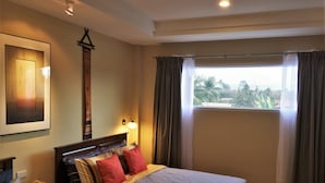 A well-lit hotel room with a large bed, a bedside table with a lamp, a window with curtains, and a framed picture on the wall. - Phu View Hideaway (Kantharalak)