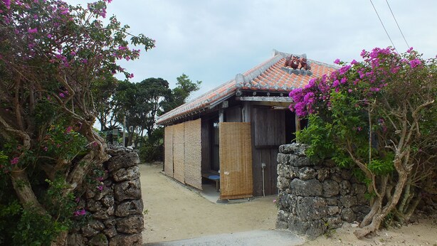 A traditional Japanese-style building with a tiled roof and a stone wall entrance. - Kohamaso (Taketomi)