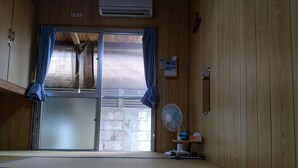 A tatami mat room with a sliding door, a fan, and a small shelf with items. - Kohamaso (Taketomi)