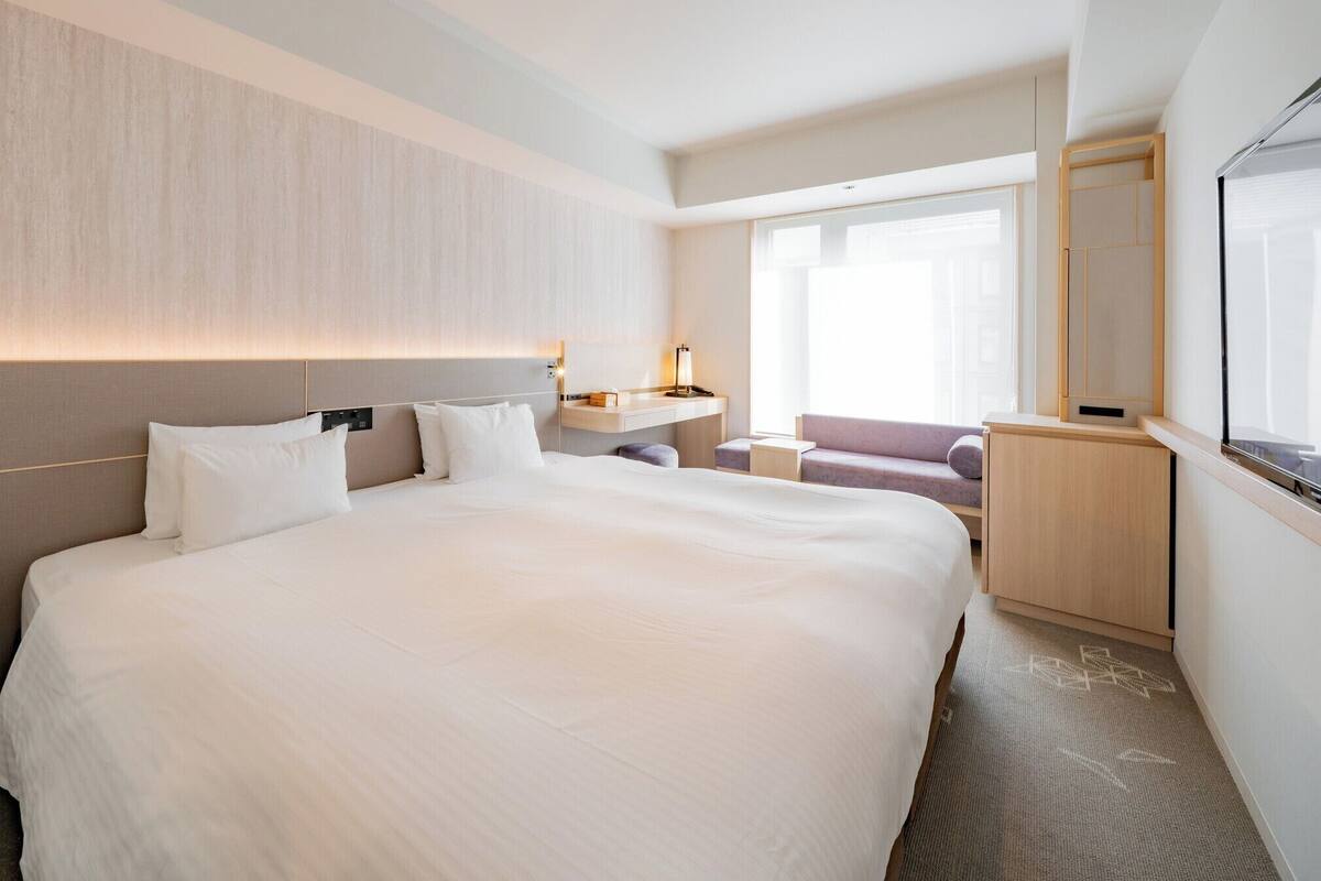 Une chambre d’hôtel moderne avec un grand lit, des tables de chevet, un bureau et une fenêtre donnant sur un beau paysage.