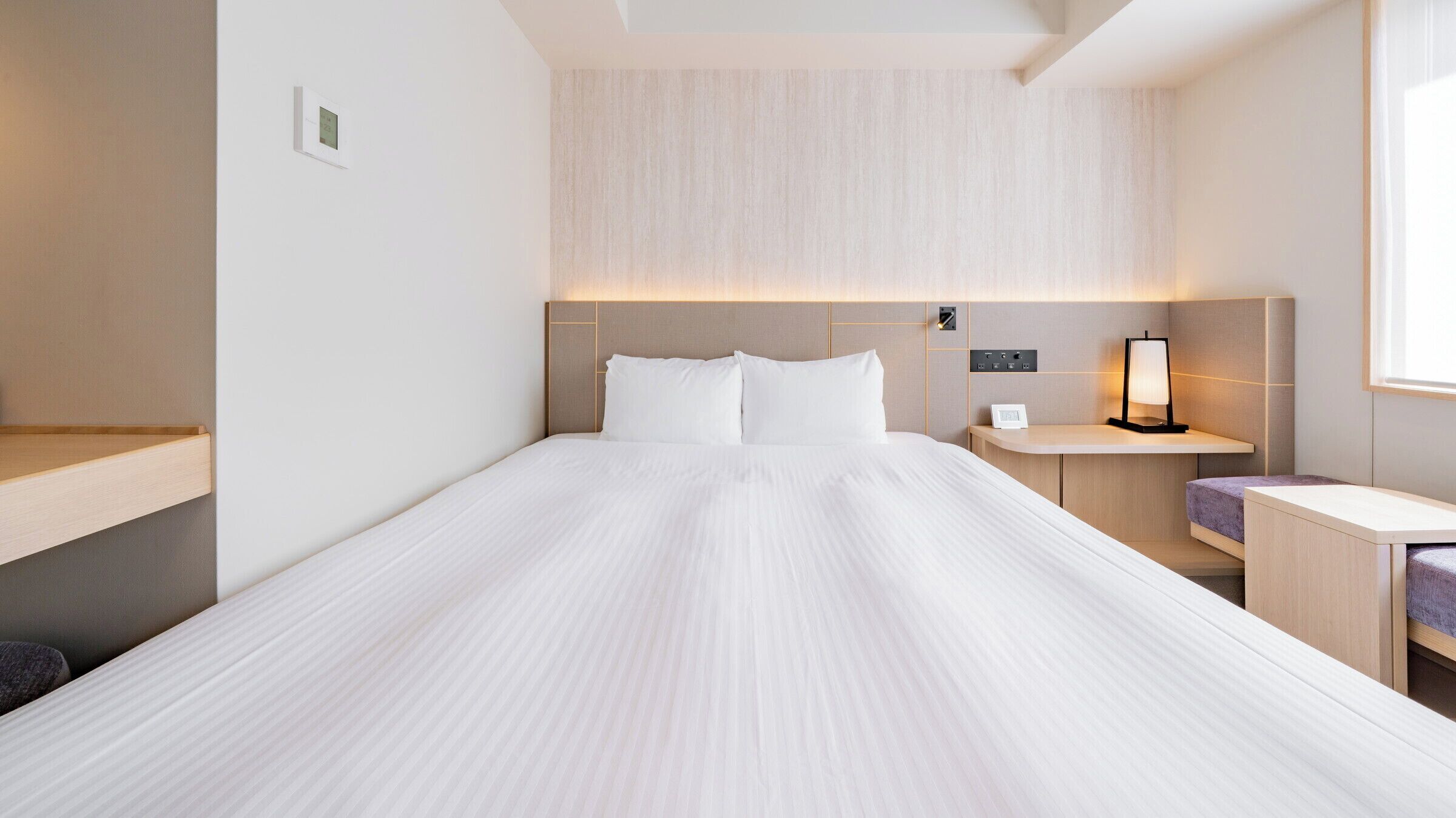 Quarto de hotel moderno com uma cama grande, mesas de cabeceira e uma janela.
