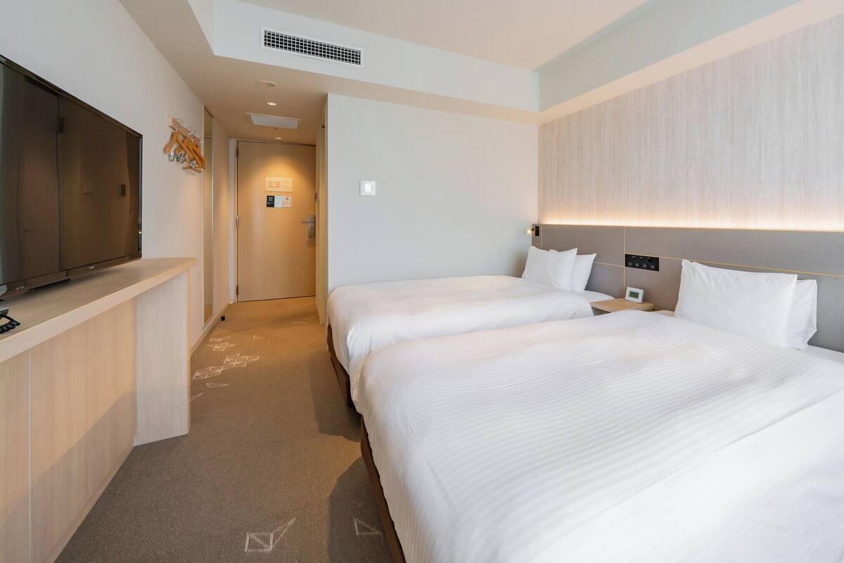 Une chambre d’hôtel avec deux lits, une télévision, une table de chevet et une porte de salle de bain.