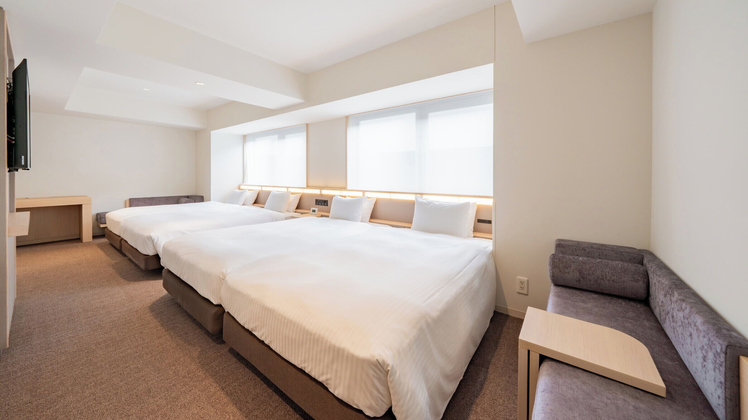 Habitación de hotel con dos camas, un sofá, televisión y ventanas amplias.
